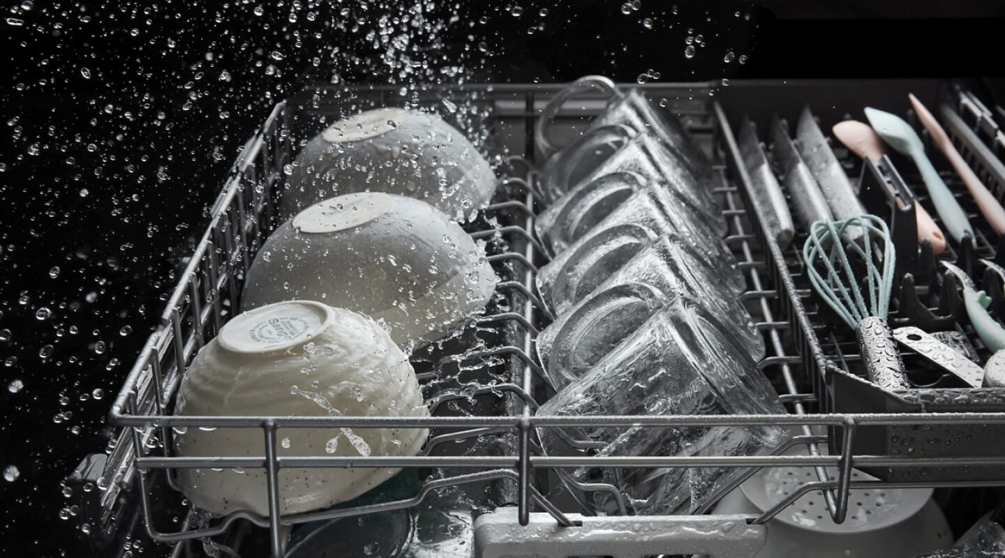 A dishwasher rack of bowls and mugs in the middle of a wash cycle A dishwasher rack of bowls and mugs in the middle of a wash cycle