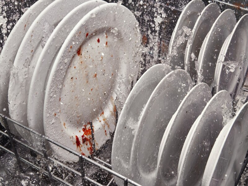 A rack of dirty dishes in the middle of a wash cycle A rack of dirty dishes in the middle of a wash cycle