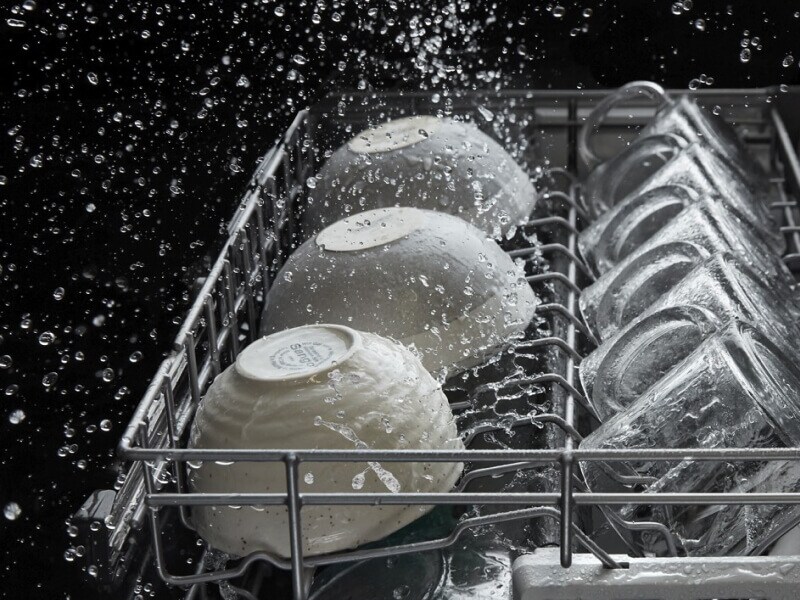 A dishwasher rack of bowls and mugs in the middle of a wash cycle A dishwasher rack of bowls and mugs in the middle of a wash cycle