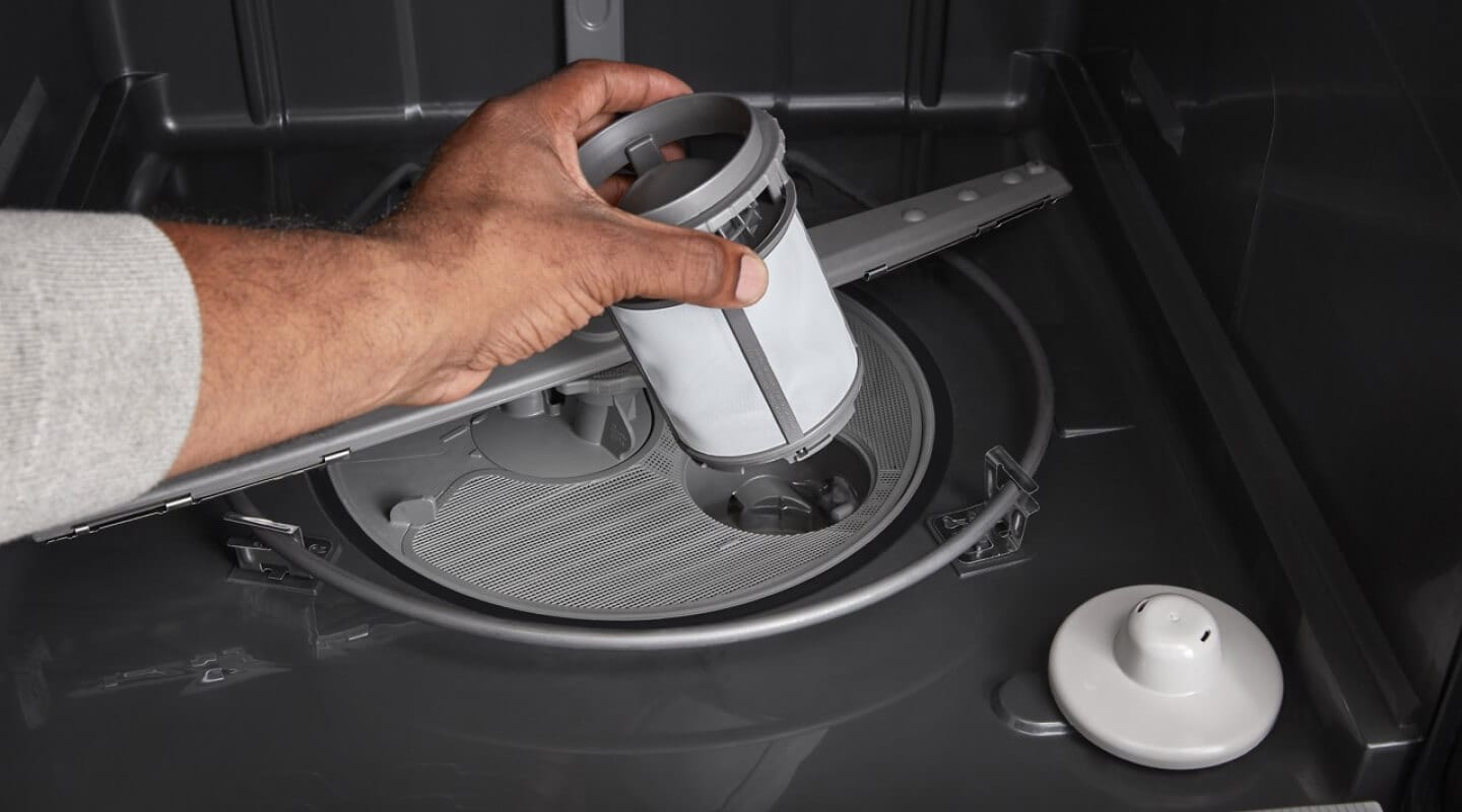 A person pulling a filter out of a dishwasher A person pulling a filter out of a dishwasher