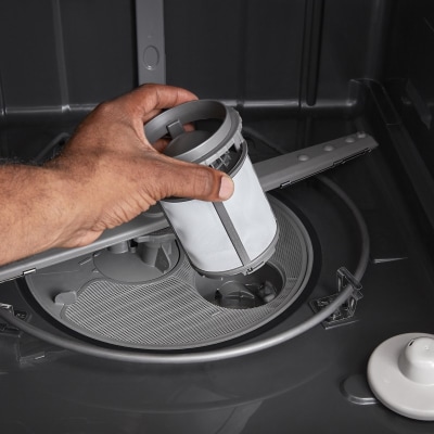 A person pulling a filter out of a dishwasher A person pulling a filter out of a dishwasher