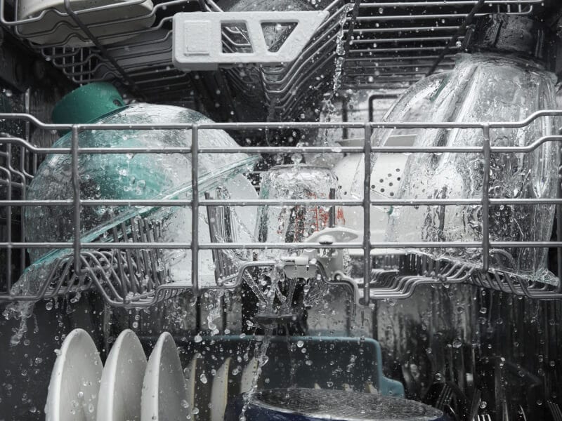 Dishes being rinsed with water inside a dishwasher