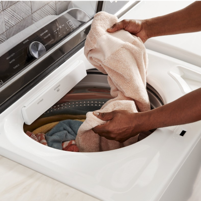 Person loading towels into a white top-load washer