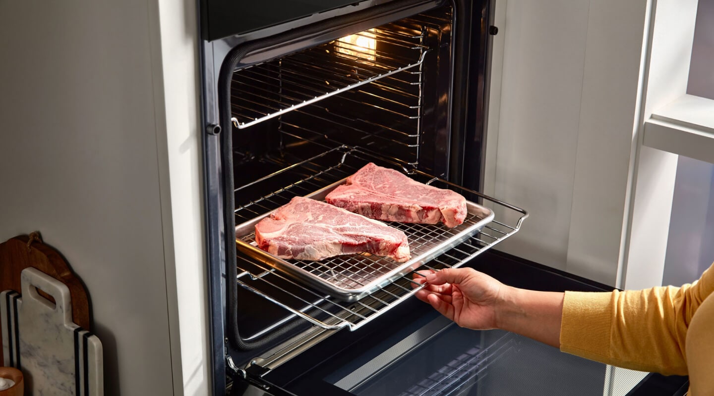 Person putting two steaks in a Whirlpool® wall oven Person putting two steaks in a Whirlpool® wall oven