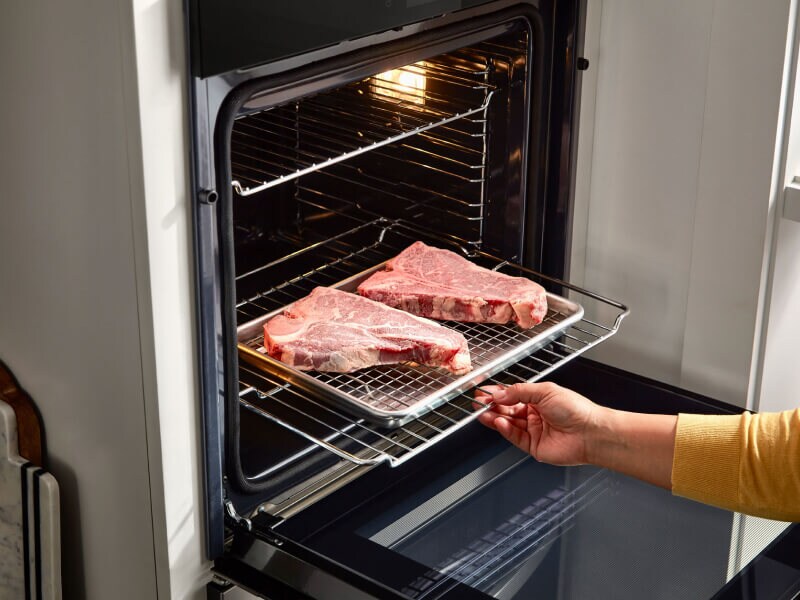 Person putting two steaks in a Whirlpool® wall oven Person putting two steaks in a Whirlpool® wall oven