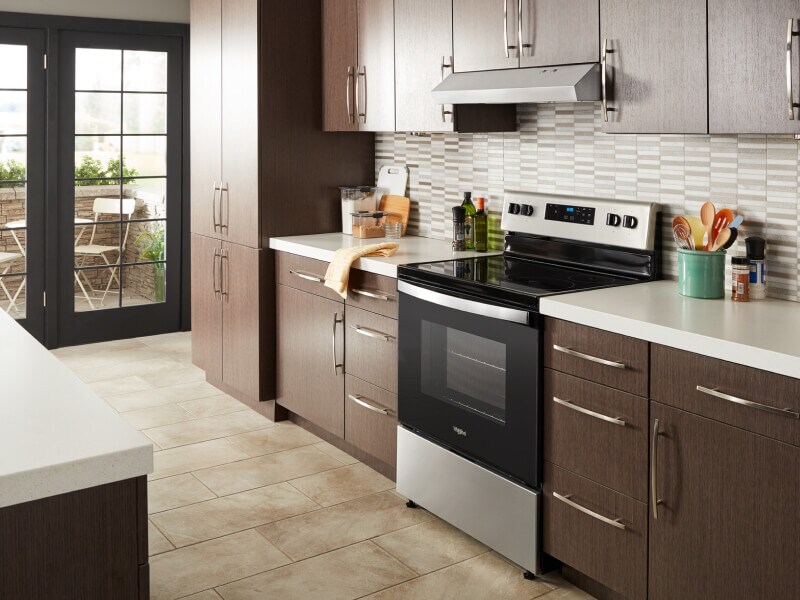 Whirlpool® electric range in a modern kitchen with a range hood above Whirlpool® electric range in a modern kitchen with a range hood above