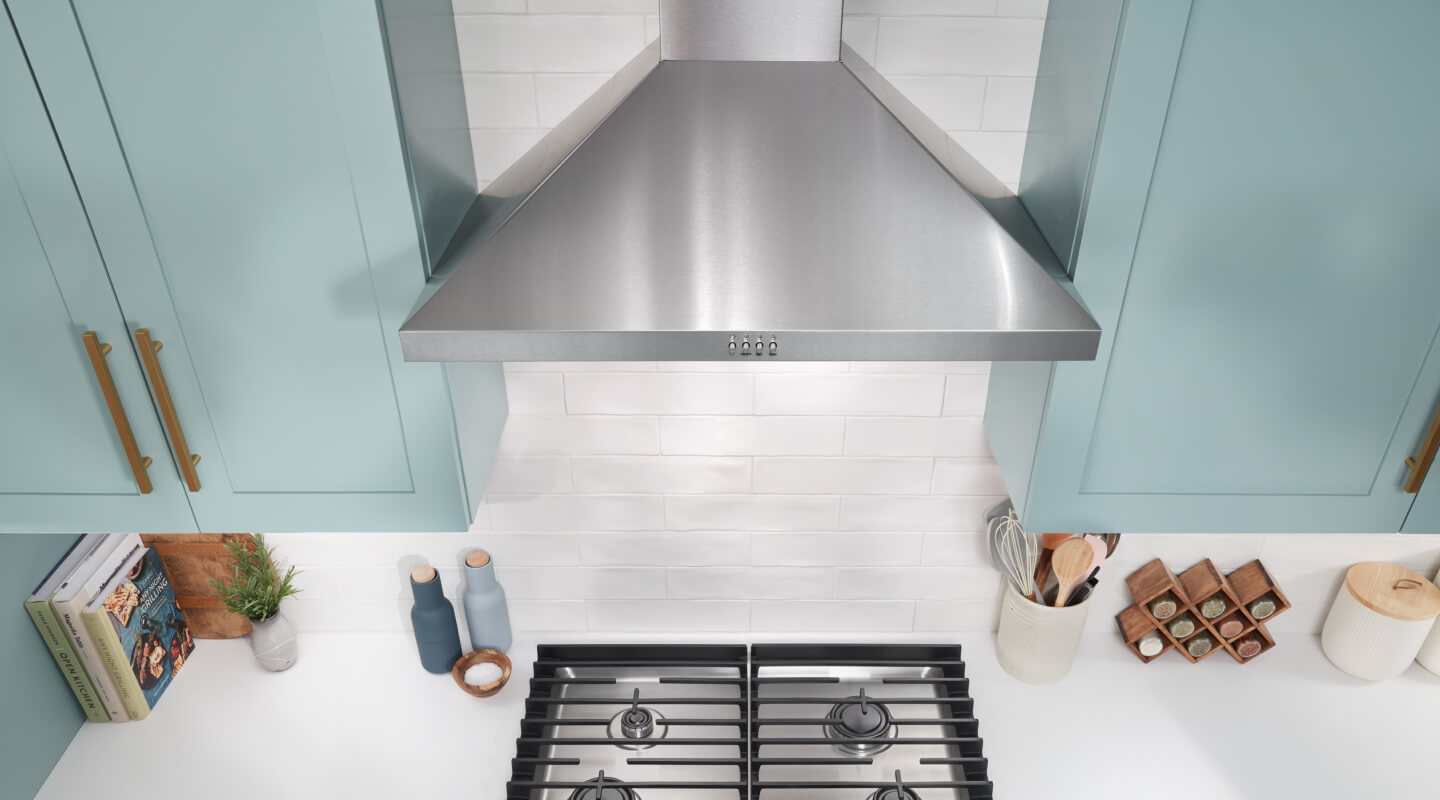 Stainless steel wall mount range hood above a gas cooktop