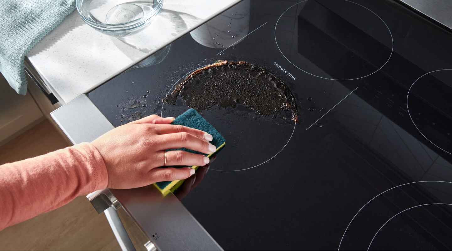 Person cleaning a spill on an electric cooktop Person cleaning a spill on an electric cooktop