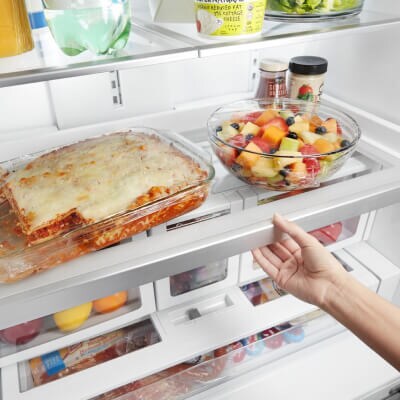 Person adjusting a shelf with lasagna and a bowl of berries on top