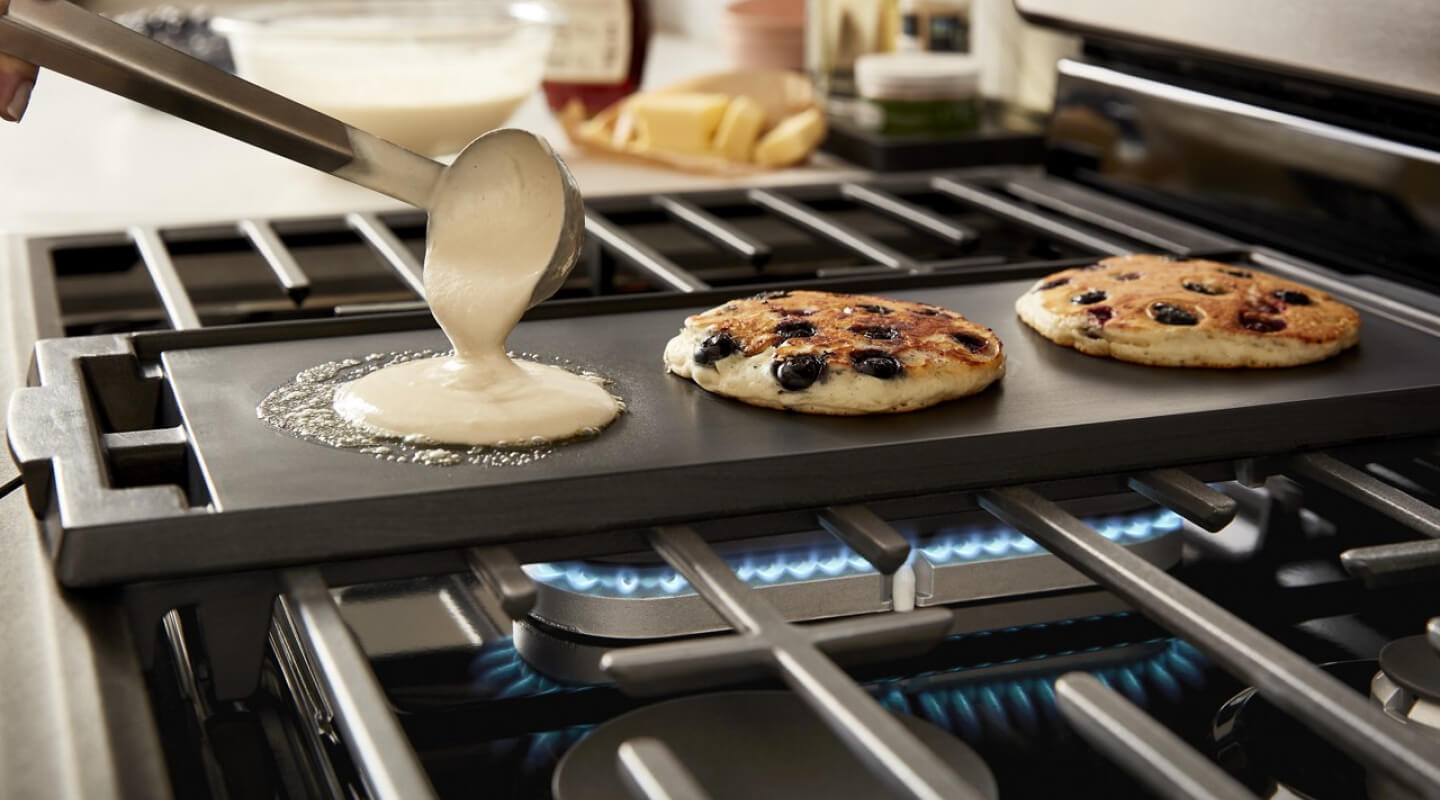 A person making blueberry pancakes on a griddle on top of a Whirlpool® Gas Range cooktop A person making blueberry pancakes on a griddle on top of a Whirlpool® Gas Range cooktop