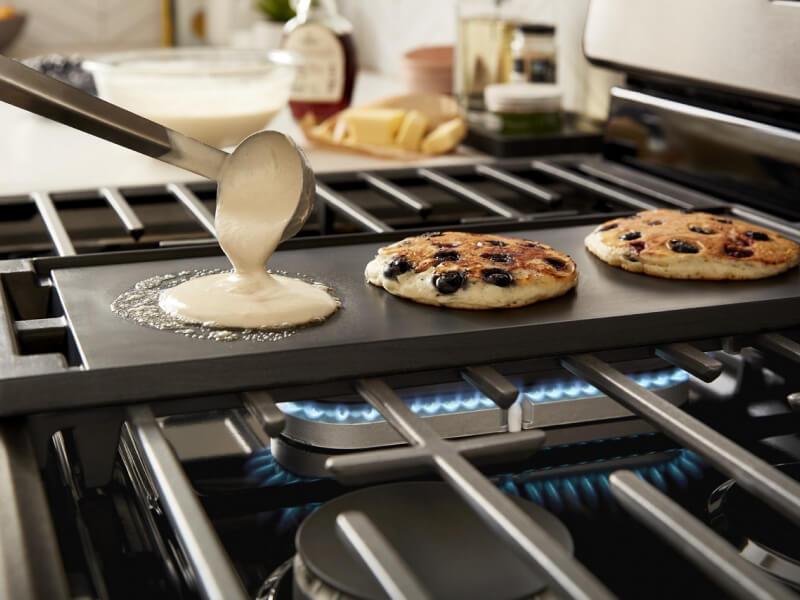 A person making blueberry pancakes on a griddle on top of a Whirlpool® Gas Range cooktop A person making blueberry pancakes on a griddle on top of a Whirlpool® Gas Range cooktop