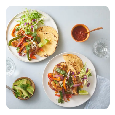 Two white dinner plates with fajitas and a side of avocado and salsa Two white dinner plates with fajitas and a side of avocado and salsa