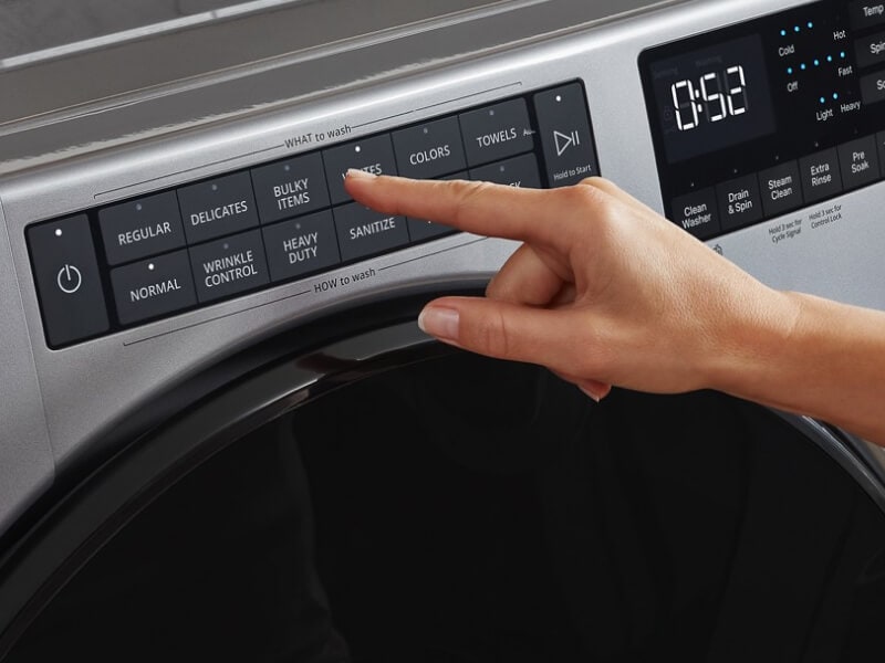 A person selecting washer settings on a control panel