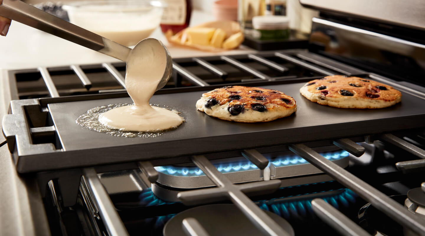 Someone making pancakes on a griddle over a gas burner