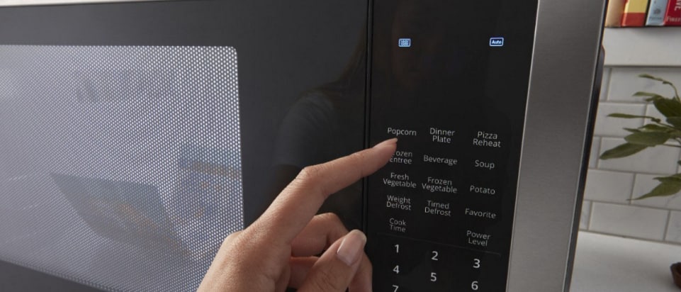 A hand selecting a popcorn setting on a microwave A hand selecting a popcorn setting on a microwave