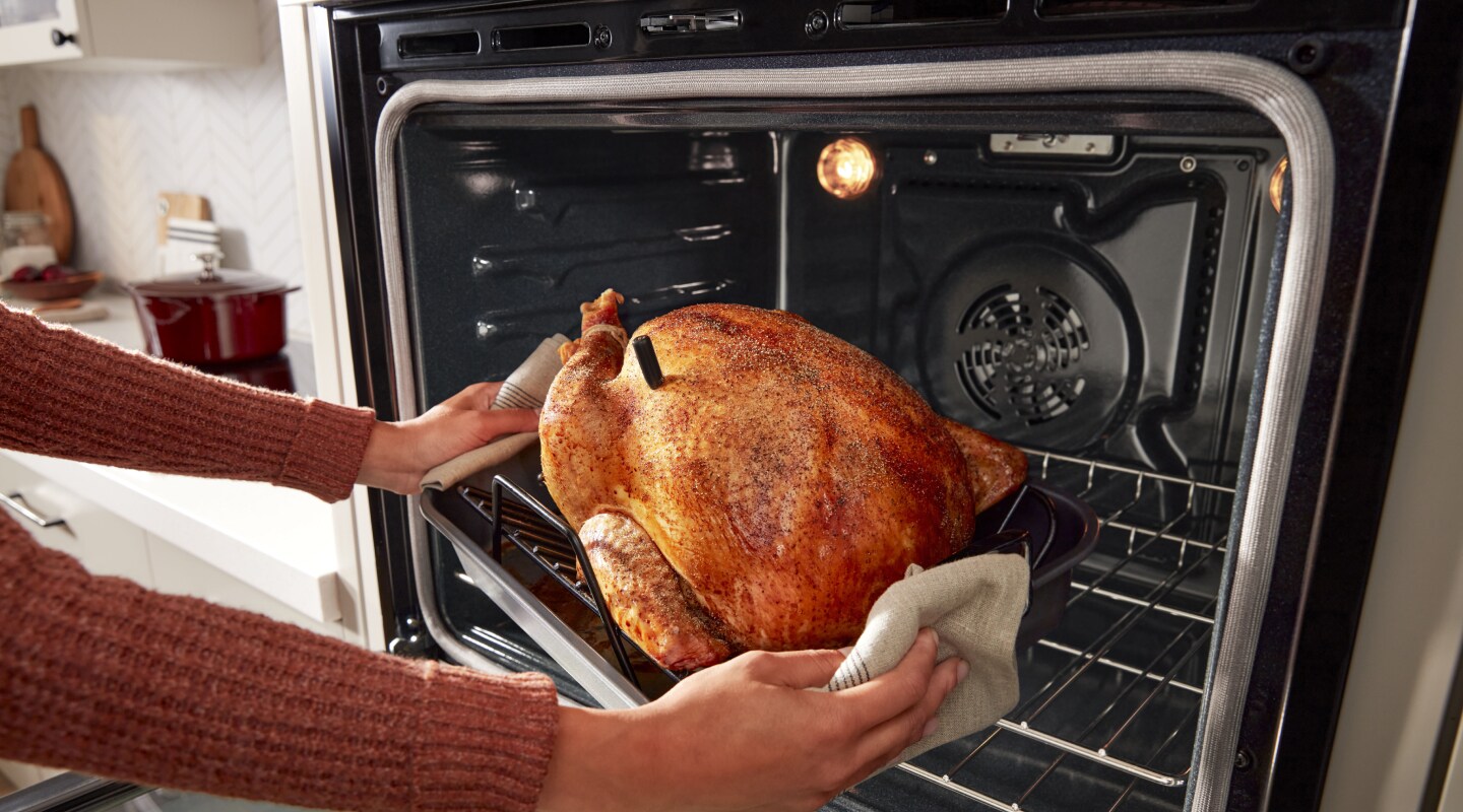 Person using oven mitts to pull a roasted turkey from the oven Person using oven mitts to pull a roasted turkey from the oven