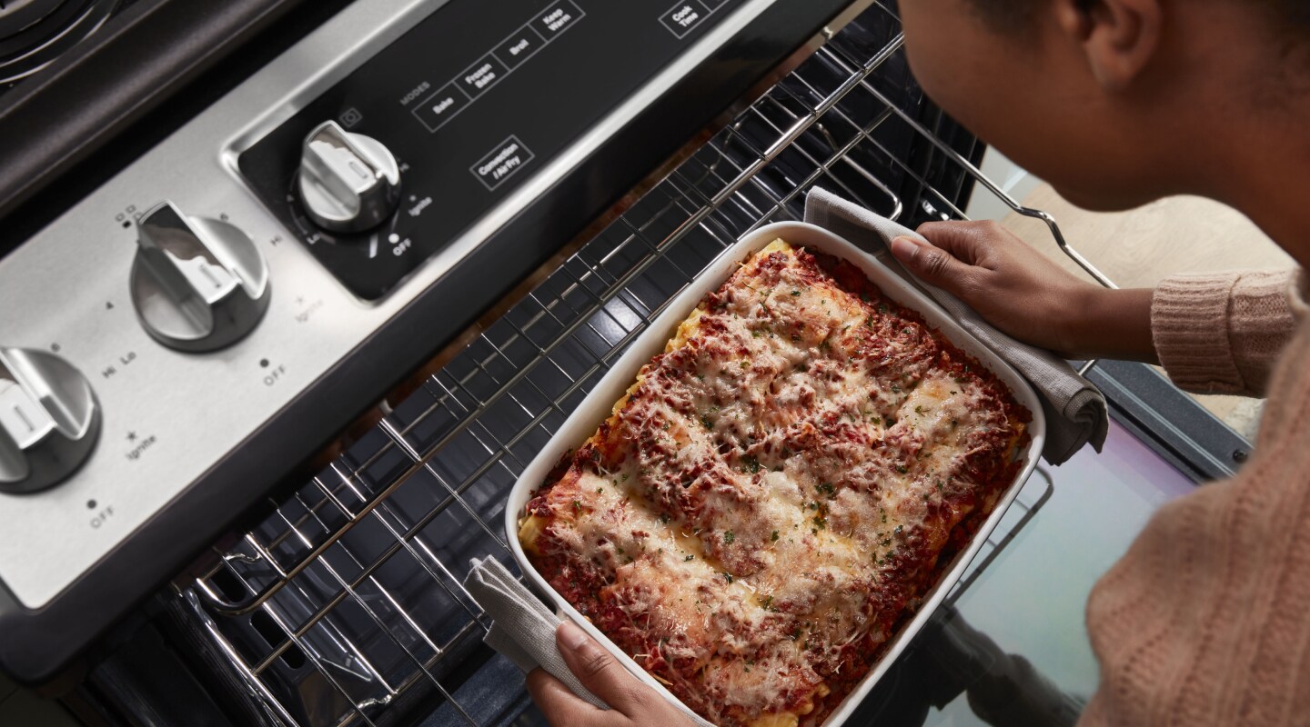 Top view of a person pulling casserole out of the top rack of an oven Top view of a person pulling casserole out of the top rack of an oven