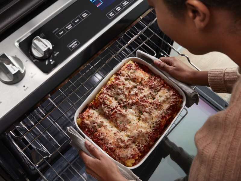 Top view of a person pulling casserole out of the top rack of an oven Top view of a person pulling casserole out of the top rack of an oven