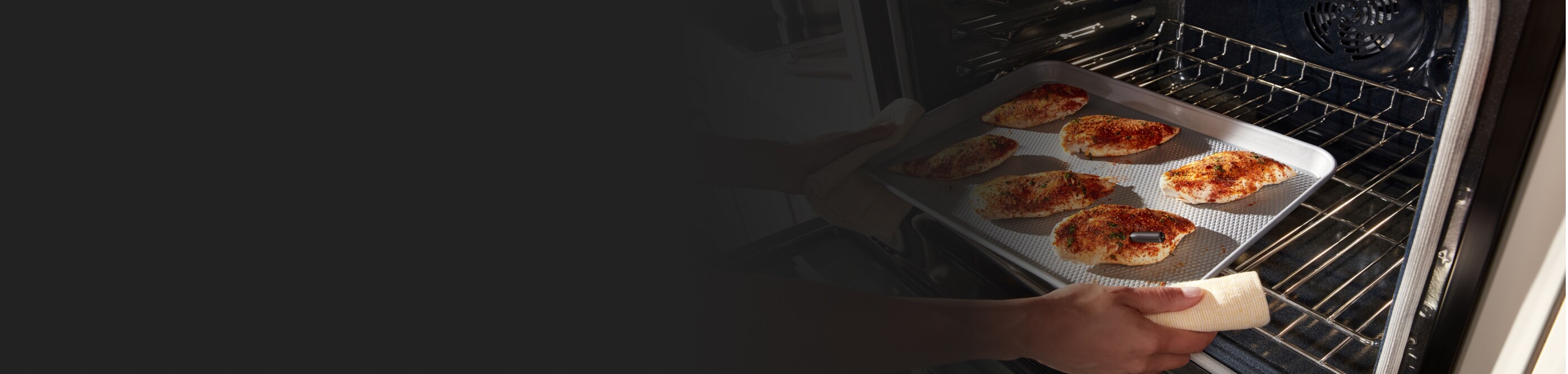 Person pulling spiced chicken breasts from an oven