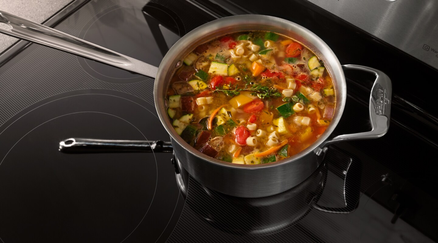 A pot of vegetable soup on a ceramic glass stovetop. A pot of vegetable soup on a ceramic glass stovetop.