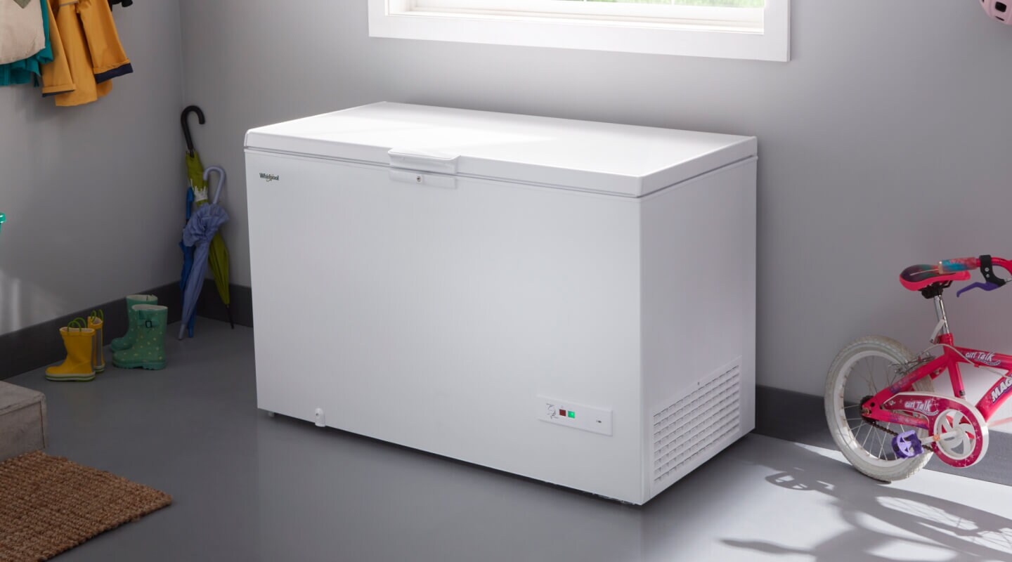 A deep freezer in a garage next to a bicycle and umbrellas