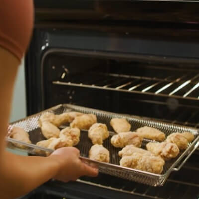 A person putting breaded chicken wings into an oven