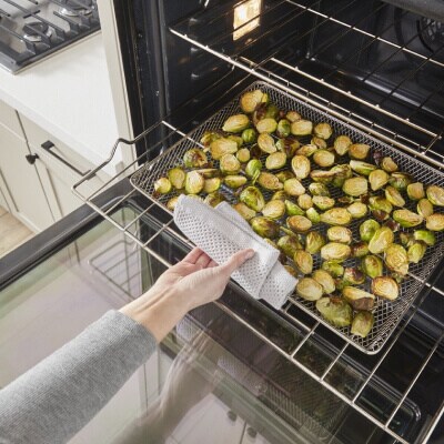 Person removing Brussels sprouts from an oven