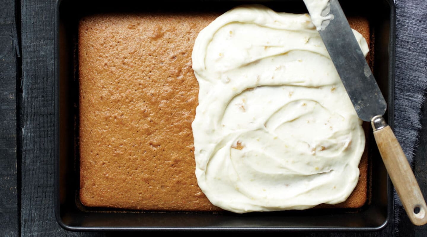A pan cake with frosting on the right half and a knife balanced on top A pan cake with frosting on the right half and a knife balanced on top