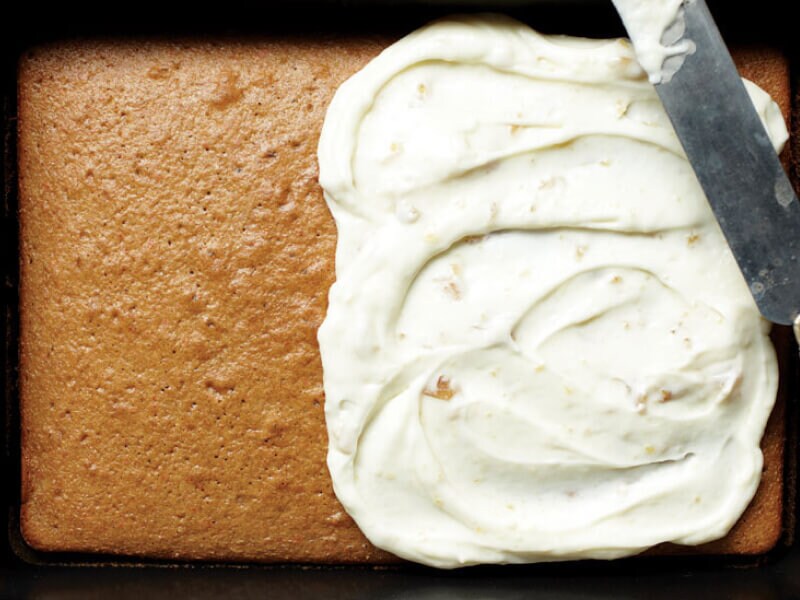 A pan cake with frosting on the right half and a knife balanced on top A pan cake with frosting on the right half and a knife balanced on top