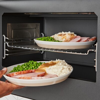 Person placing plates of ham, peas and mashed potatoes into a microwave