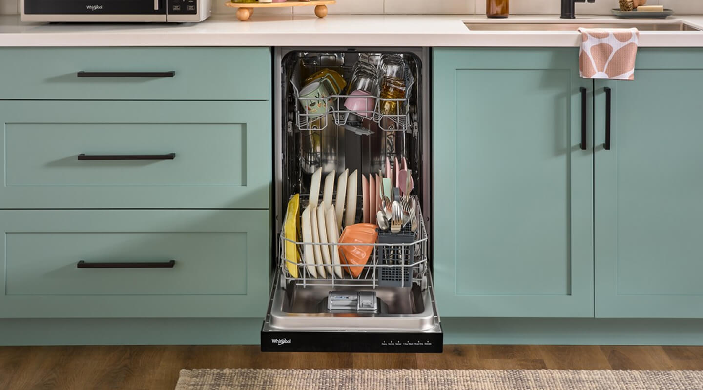 Small dishwasher open and full of dishes between blue cabinets
