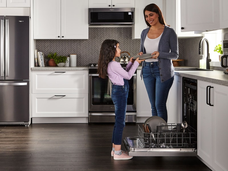 Person handing a child a clean dish in a kitchen Person handing a child a clean dish in a kitchen