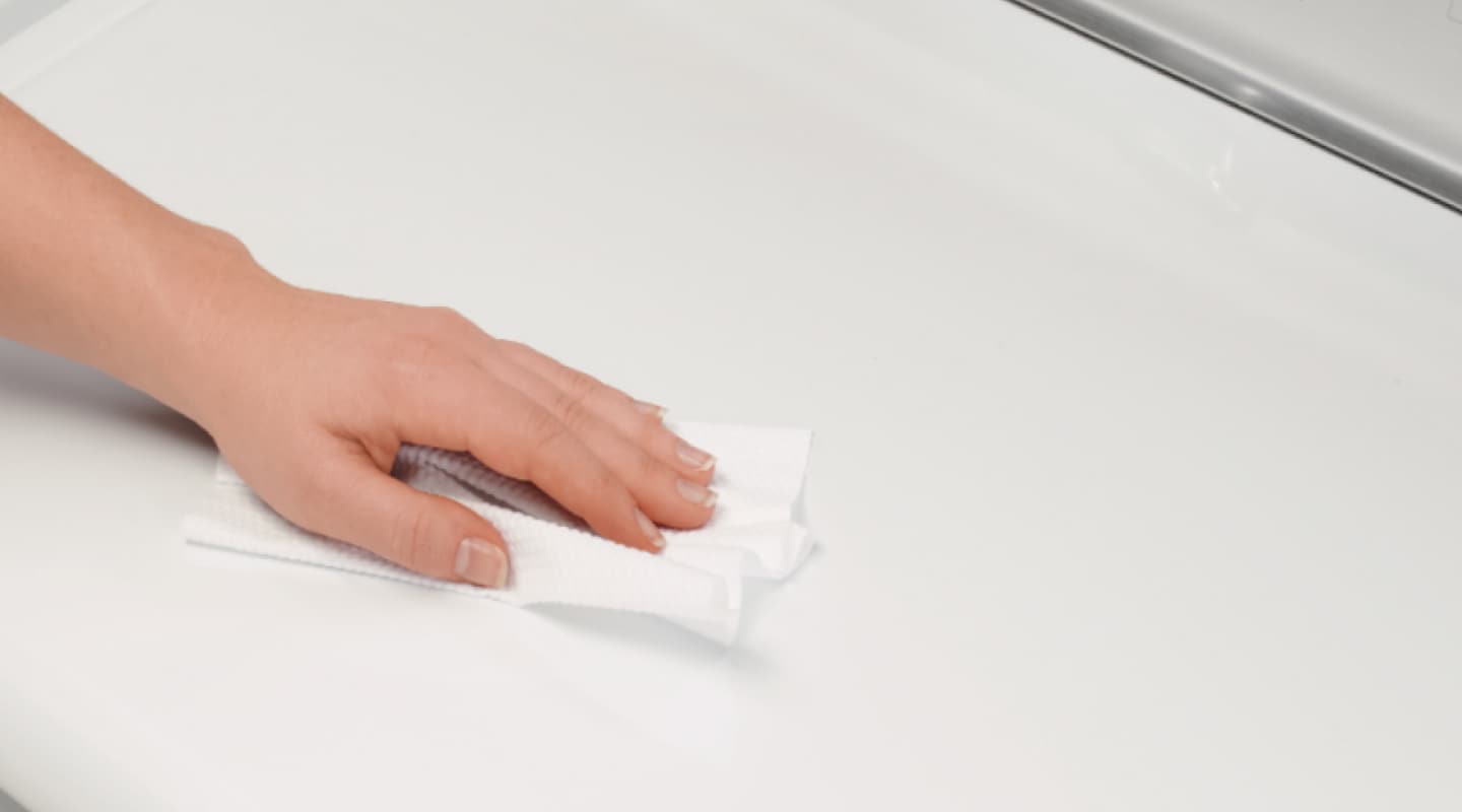 Hand wiping top of white dryer.
