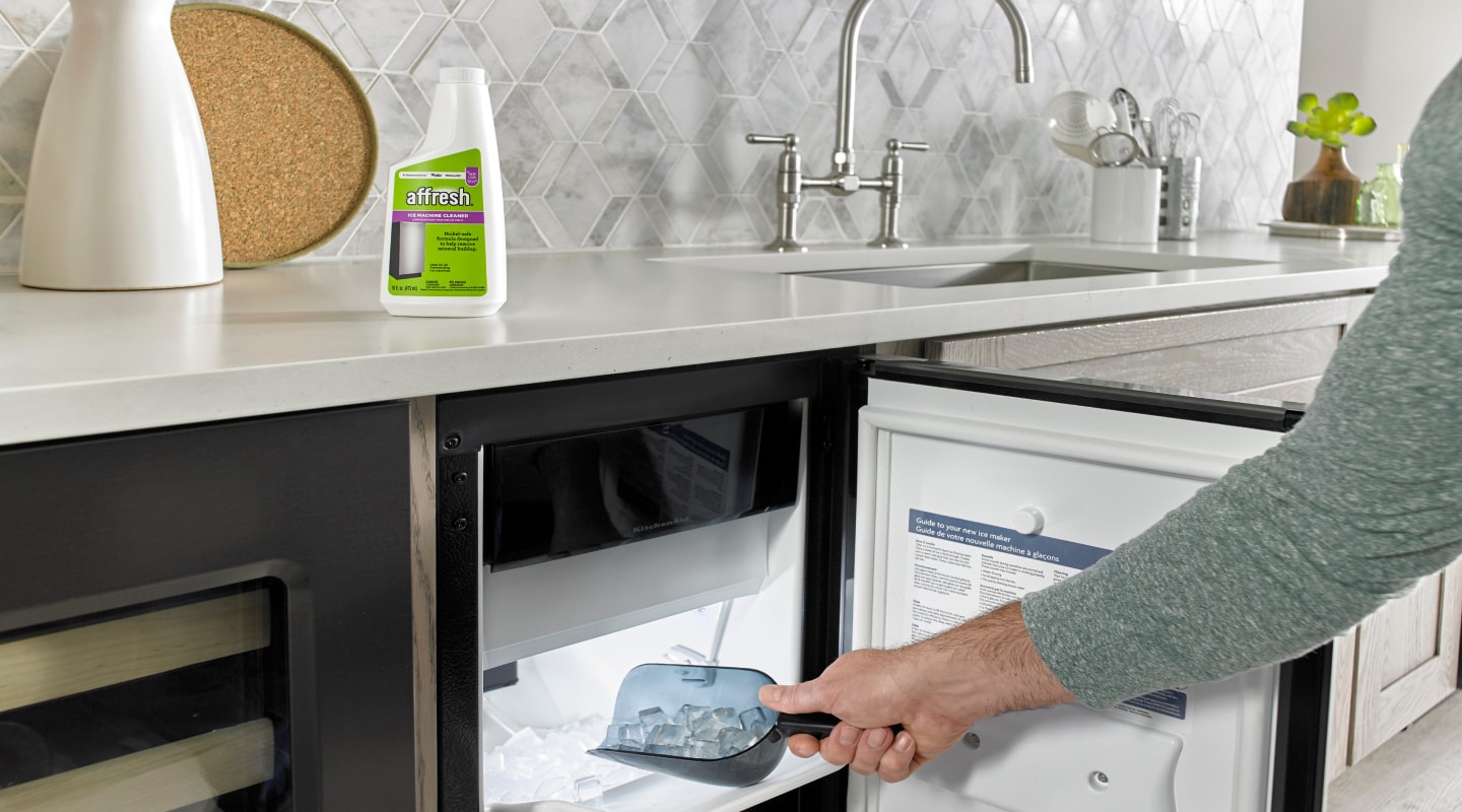 A hand scooping ice from an open ice maker