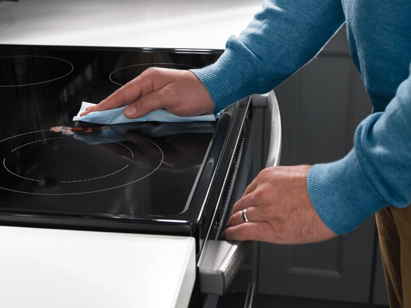 A hand wiping the cooking surface of an electric range
