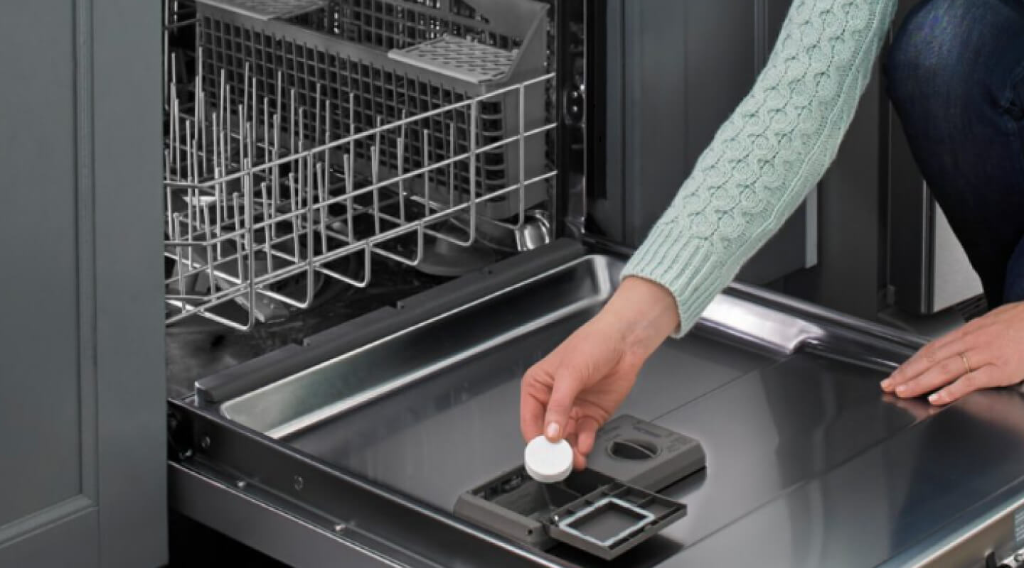 A person adding a dishwasher cleaner tablet to a dishwasher