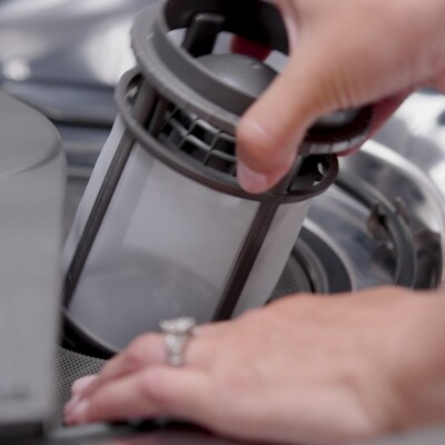 A person removing a filter from a dishwasher