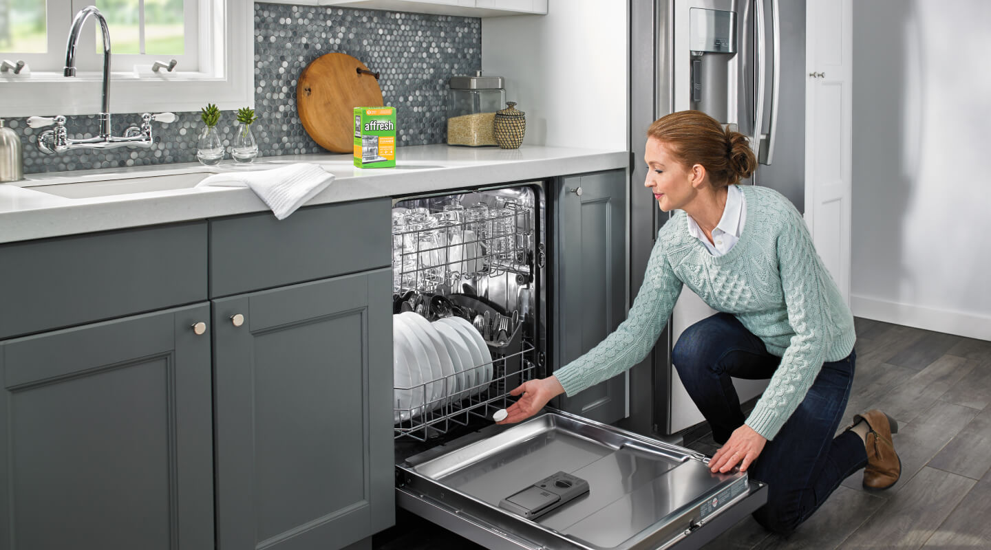 Person adding a cleaning tablet to the bottom of an open and loaded dishwasher