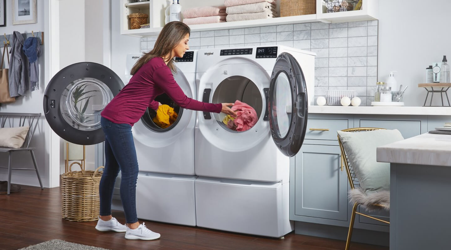 Person moving clothes between a matching Whirlpool® Front Load Washer and dryer