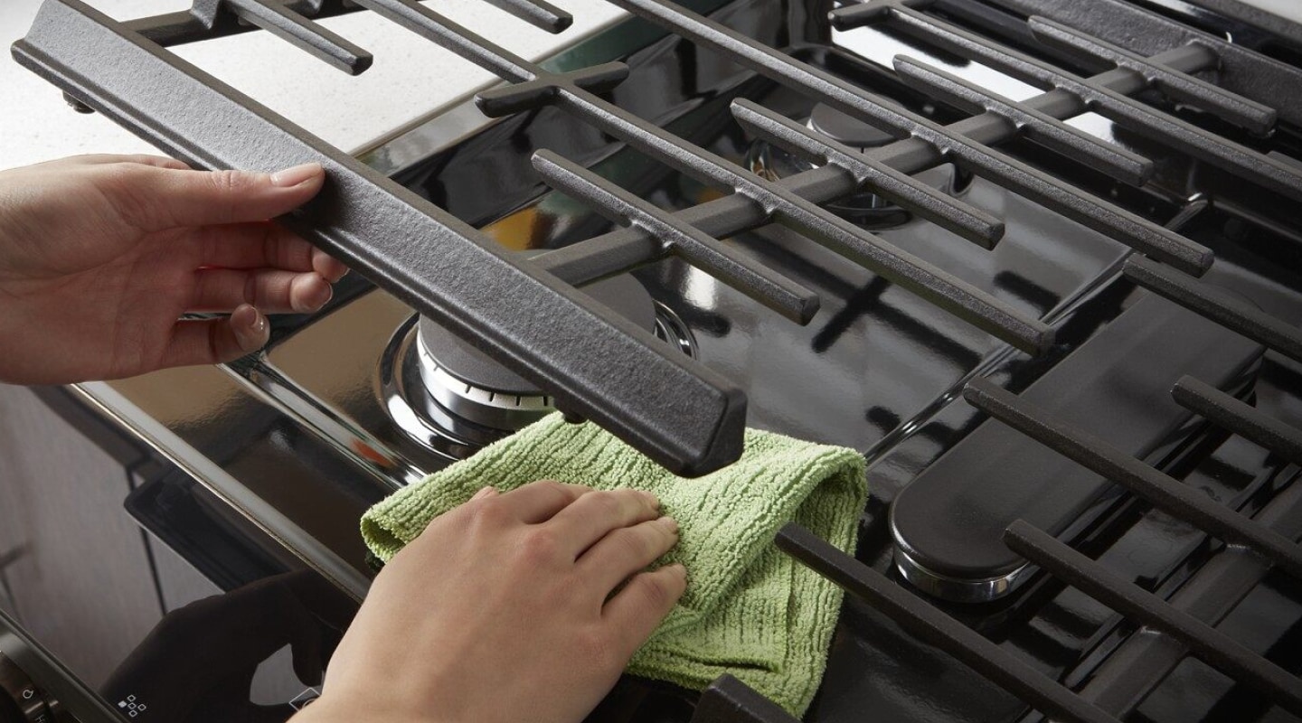 A person lifting up stove grates to clean underneath. A person lifting up stove grates to clean underneath.