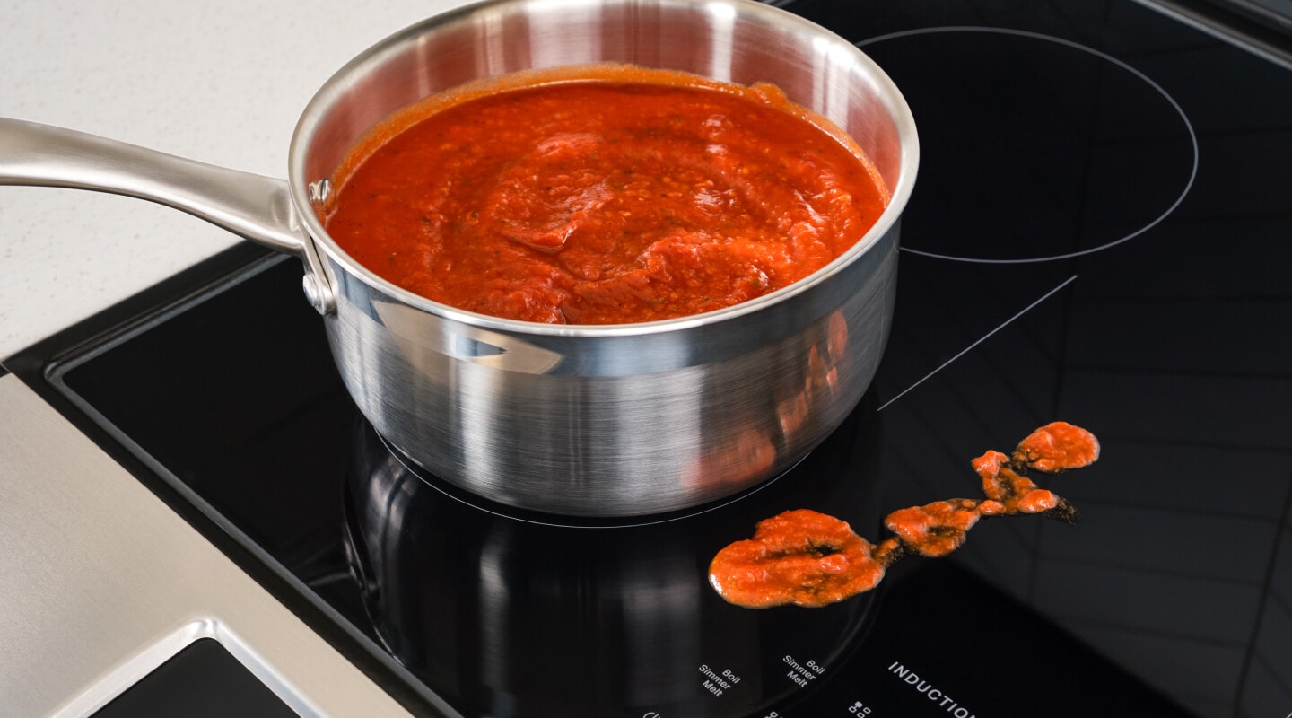 Sauce in a pan on an induction stovetop, next to splatter on the stovetop Sauce in a pan on an induction stovetop, next to splatter on the stovetop
