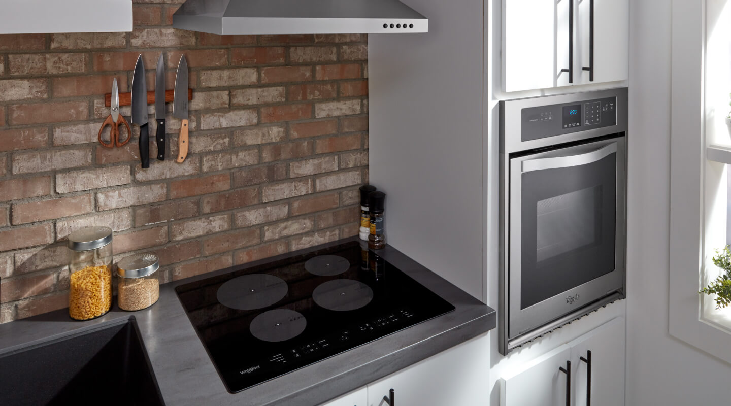 Induction stovetop next to a wall oven in white cabinetry
