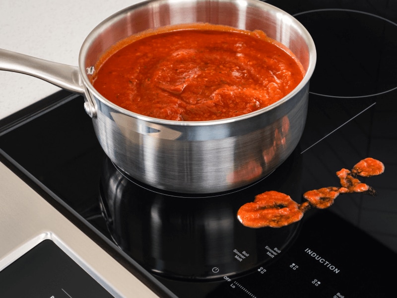 Sauce in a pan on an induction stovetop, next to splatter on the stovetop Sauce in a pan on an induction stovetop, next to splatter on the stovetop