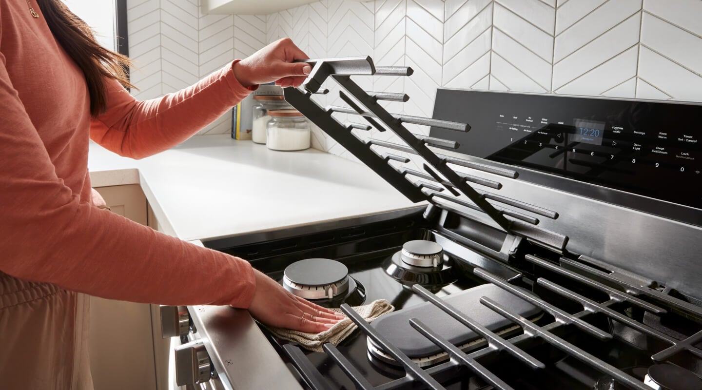 Hand lifting the grill covering a burner to clean beneath it