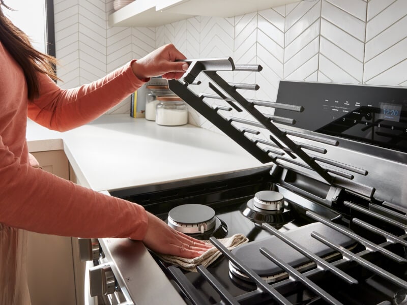 Hand lifting the grill covering a burner to clean beneath it