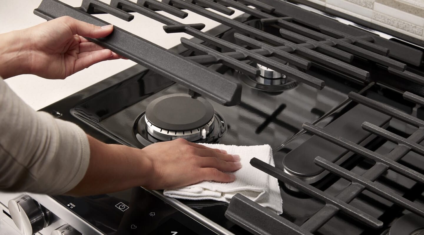 Person lifting grates to clean gas stovetop