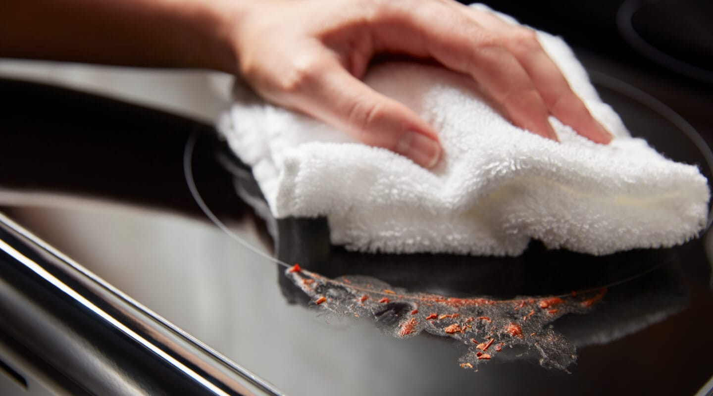 Person cleaning a mess on an electric cooktop Person cleaning a mess on an electric cooktop