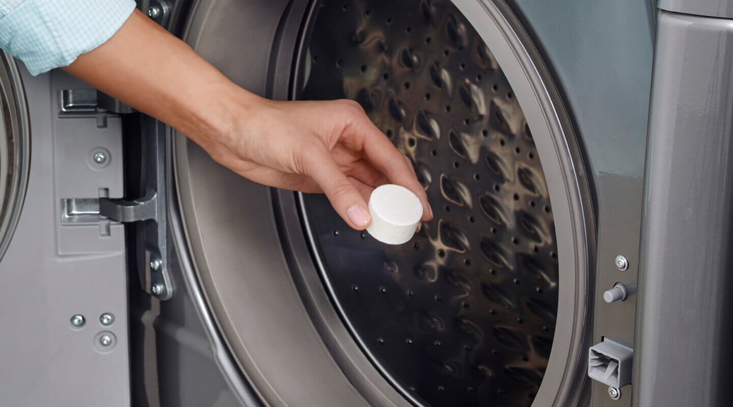 Person adding a washing machine cleaner tablet to a washing machine