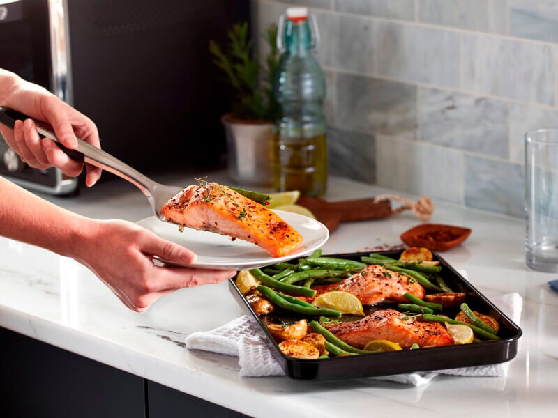 Person placing a piece of cooked salmon on a plate