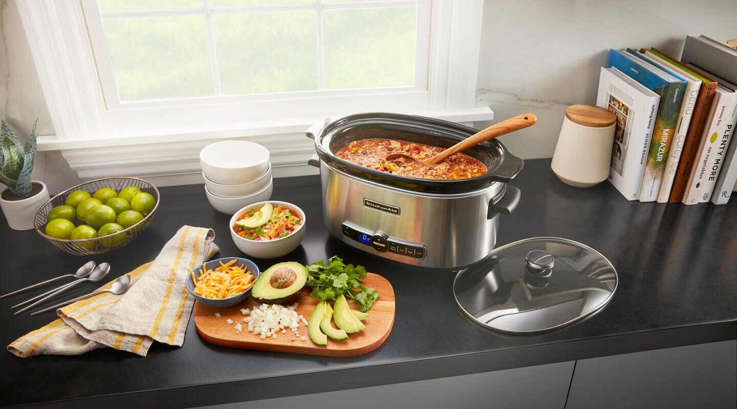 Slow cooker filled with chili next to a cutting board with toppings